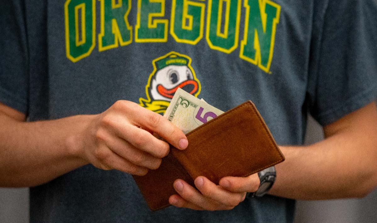 Student wearing a grey t-shirt with Oregon in green letters taking money from a wallet